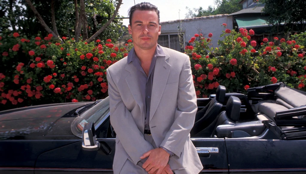 Marcus Tandy in a grey suit leaning against his sports car